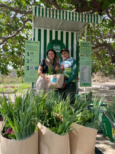 Imagem de Gleicy e Glenda segurando plantas cultivadas na horta orgânica, que estão celebrando 24 anos da Terra Brasilis conosco